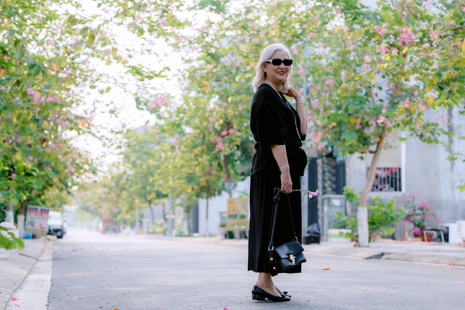 A woman walking outdoors on a sunny, tree-lined street