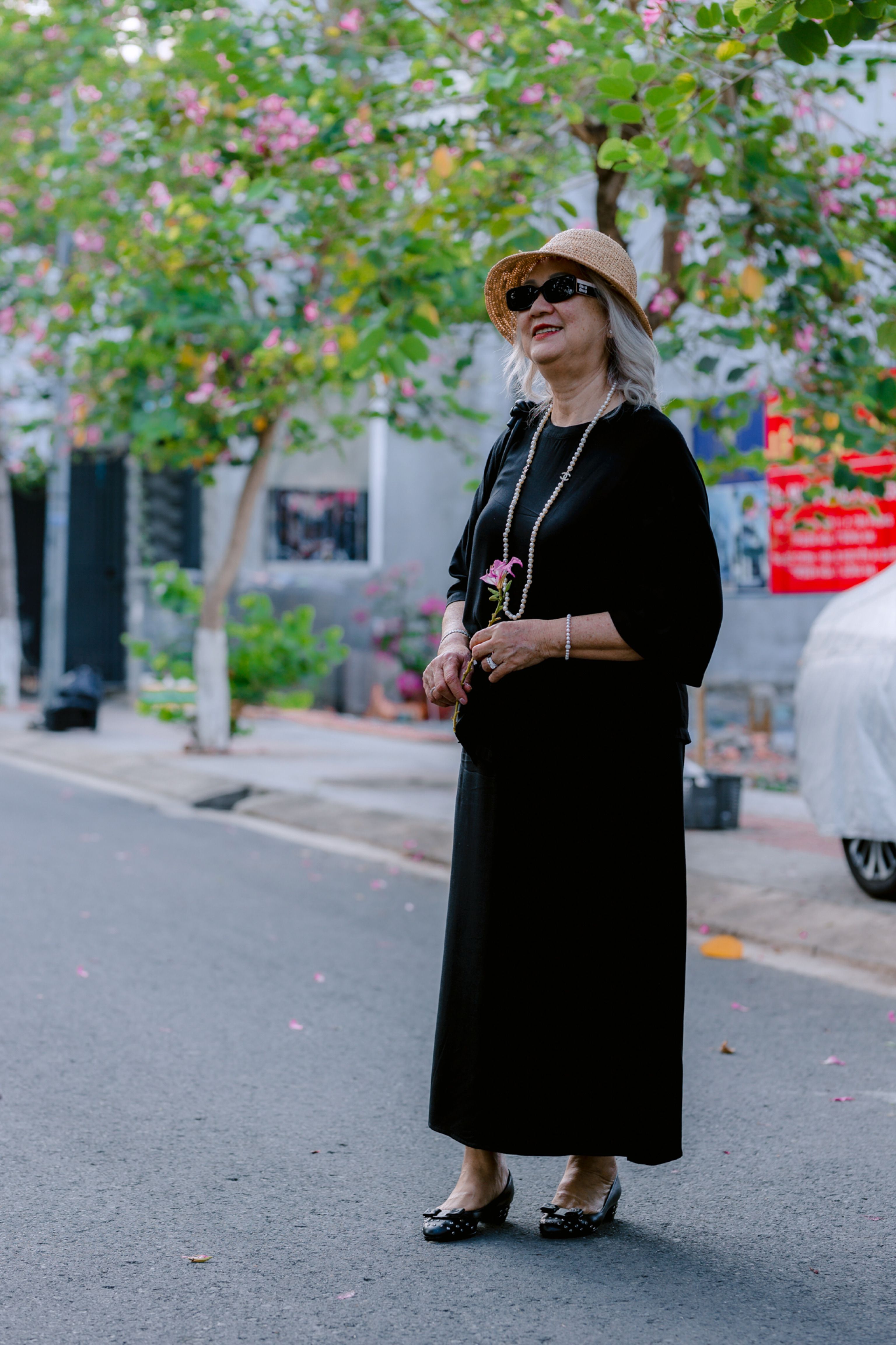 A smiling older woman in a sun hat strolling beneath blossoming trees